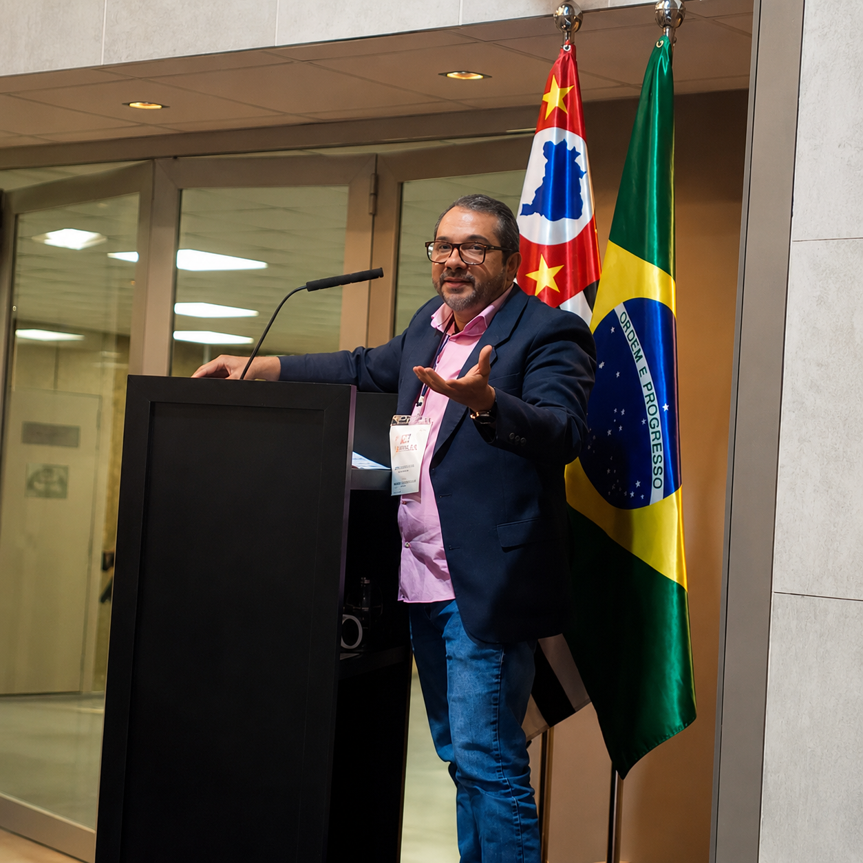 Dr. José Airton durante palestra médica, diante das bandeiras de São Paulo e do Brasil